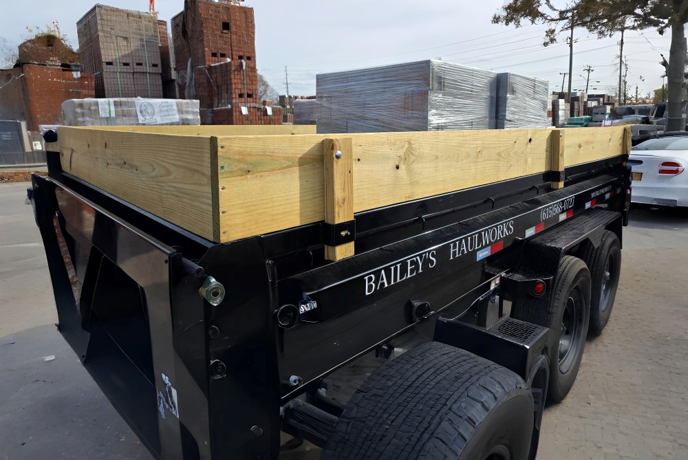 Bailey’s Haulworks team hauling a loaded dump trailer on site with equipment for rental and cleanup services